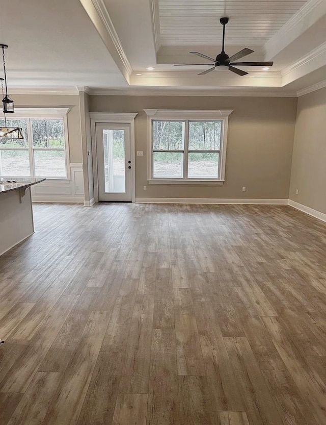 unfurnished living room with ceiling fan, a raised ceiling, wood finished floors, and ornamental molding