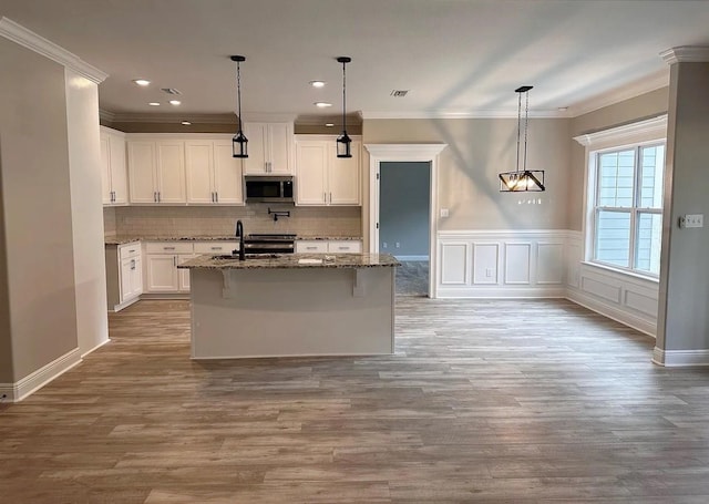 kitchen with tasteful backsplash, dark stone counters, ornamental molding, appliances with stainless steel finishes, and wood finished floors