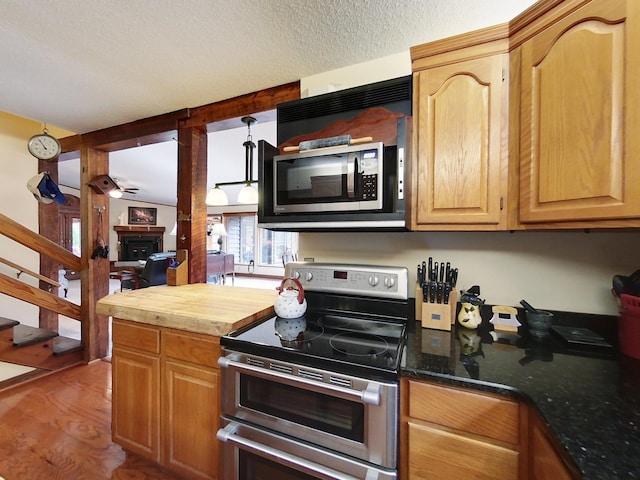 kitchen featuring ceiling fan, dark stone countertops, a textured ceiling, appliances with stainless steel finishes, and light hardwood / wood-style floors