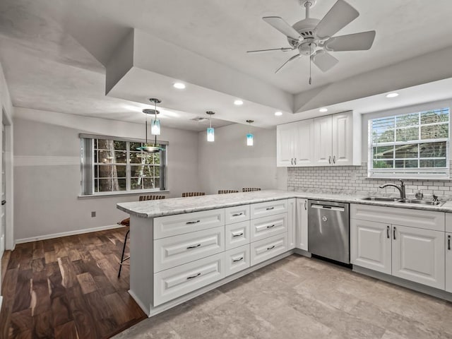 kitchen featuring dishwasher, sink, white cabinets, light stone counters, and kitchen peninsula