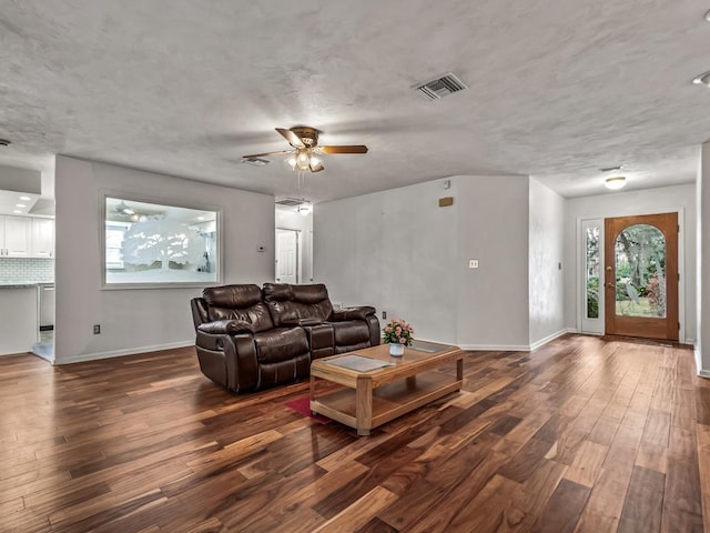 living room featuring dark wood-type flooring, ceiling fan, and a textured ceiling