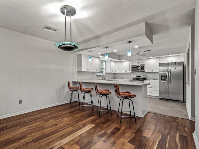 kitchen featuring dark hardwood / wood-style floors, kitchen peninsula, stainless steel appliances, decorative backsplash, and white cabinets