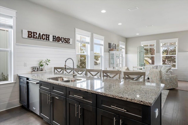 kitchen featuring sink, dishwasher, dark hardwood / wood-style floors, light stone countertops, and a center island with sink