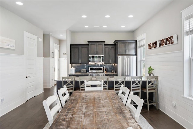 kitchen featuring dark wood-type flooring, appliances with stainless steel finishes, dark brown cabinets, light stone countertops, and a kitchen bar