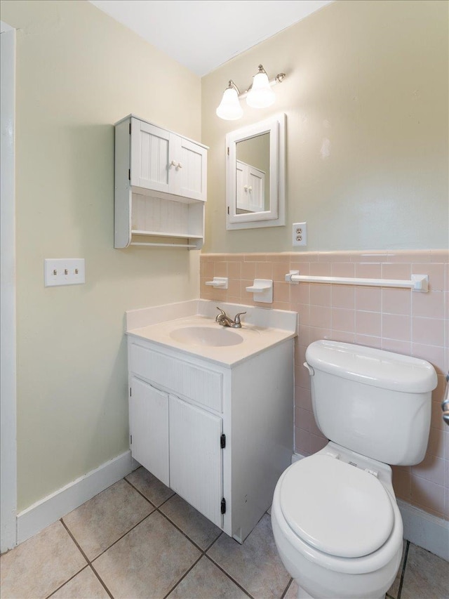 half bath with tile patterned flooring, tile walls, a wainscoted wall, toilet, and vanity