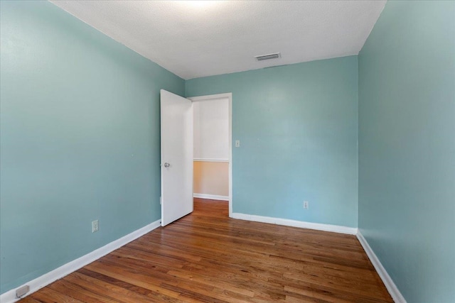 empty room featuring visible vents, baseboards, a textured ceiling, and wood finished floors