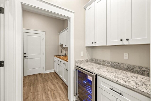 bar with wine cooler, white cabinetry, sink, and light stone counters