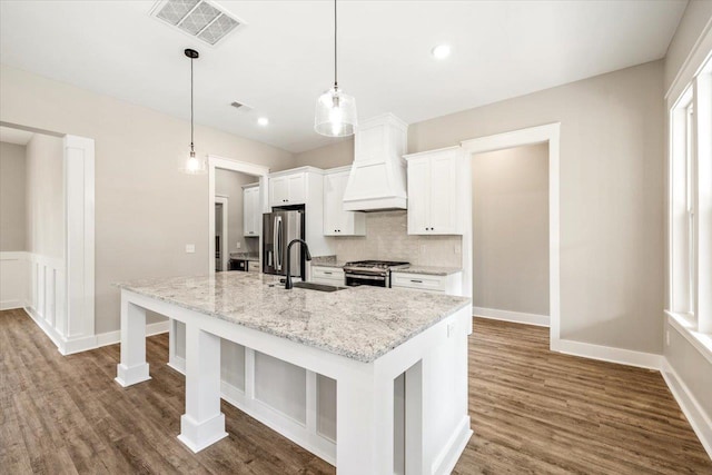 kitchen with sink, an island with sink, decorative light fixtures, white cabinets, and appliances with stainless steel finishes