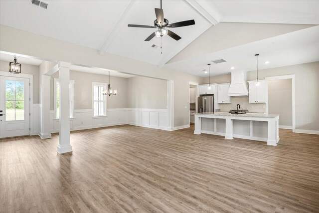 unfurnished living room featuring high vaulted ceiling, ceiling fan with notable chandelier, sink, light wood-type flooring, and beamed ceiling