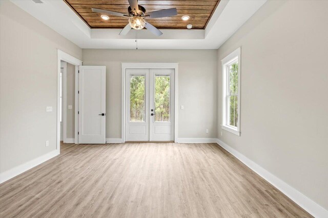 empty room featuring a healthy amount of sunlight, wooden ceiling, a tray ceiling, and french doors