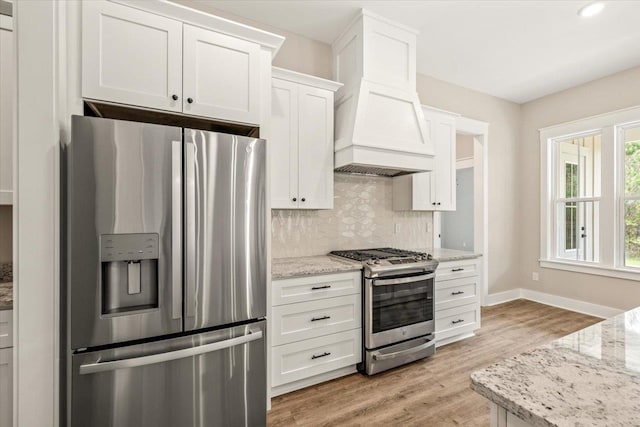 kitchen with white cabinets, appliances with stainless steel finishes, premium range hood, and light stone counters