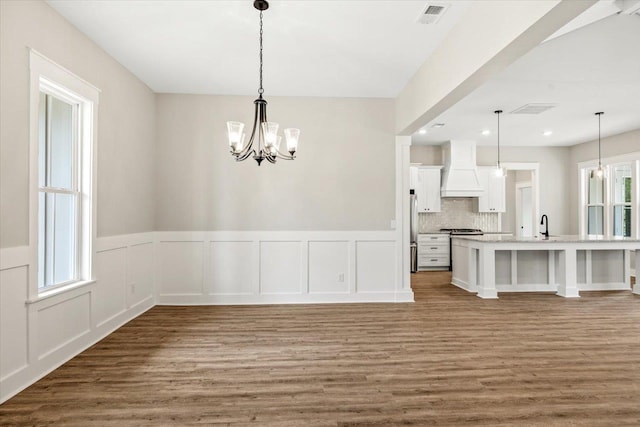 kitchen featuring custom range hood, pendant lighting, white cabinetry, and a notable chandelier