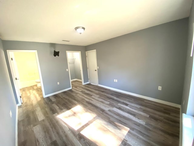 unfurnished bedroom featuring a walk in closet, dark hardwood / wood-style flooring, and a closet