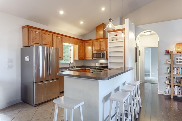 kitchen with arched walkways, stainless steel appliances, a sink, hanging light fixtures, and dark countertops