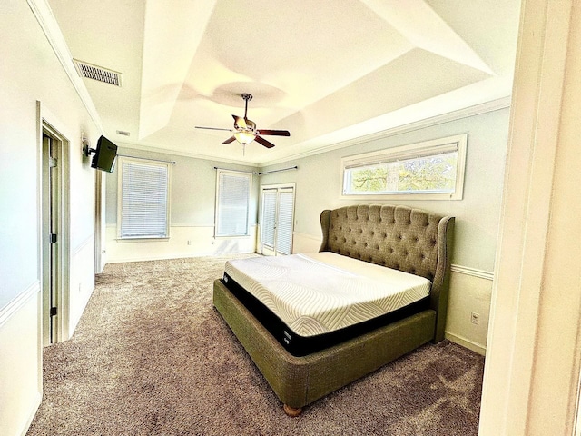 bedroom with dark colored carpet, a raised ceiling, visible vents, ornamental molding, and a ceiling fan