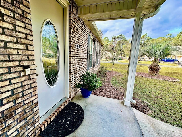 view of exterior entry with a yard and brick siding