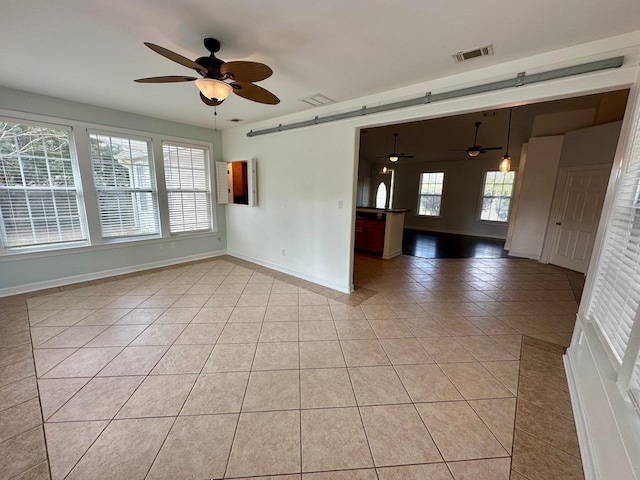 empty room featuring light tile patterned floors, a barn door, visible vents, and baseboards