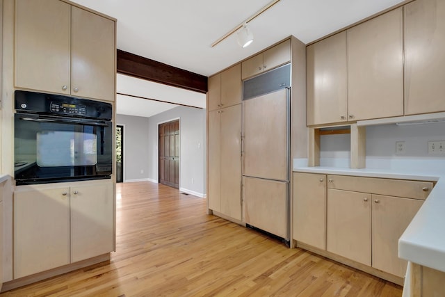 kitchen with light hardwood / wood-style floors, track lighting, black oven, paneled built in refrigerator, and cream cabinetry