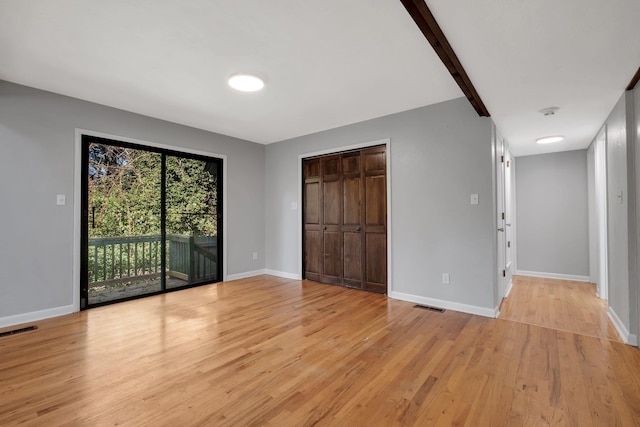 unfurnished bedroom featuring light wood-type flooring, access to outside, beamed ceiling, and a closet