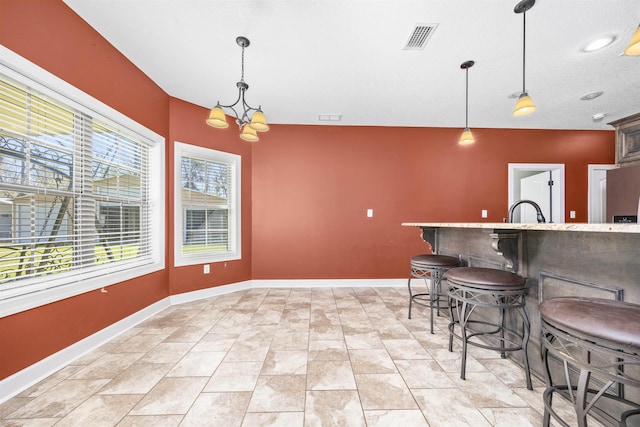 kitchen with baseboards, visible vents, a breakfast bar, decorative light fixtures, and a notable chandelier