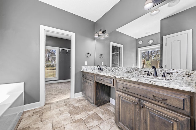 full bath featuring double vanity, a bath, baseboards, and a sink