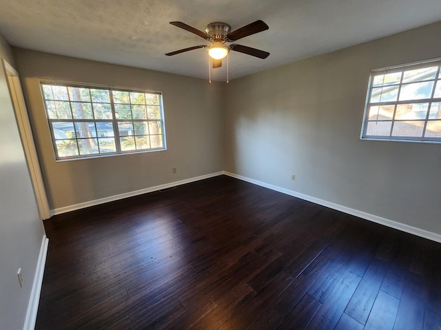 unfurnished room featuring a ceiling fan, a healthy amount of sunlight, dark wood finished floors, and baseboards