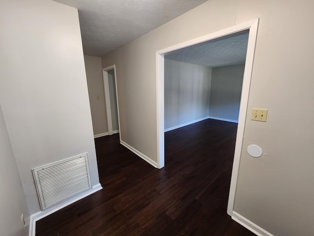 hallway with baseboards, a textured ceiling, visible vents, and wood finished floors