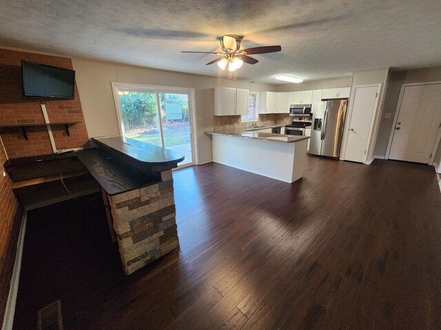 kitchen featuring dark wood-type flooring, a peninsula, stainless steel appliances, white cabinetry, and backsplash