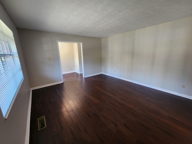 empty room featuring visible vents, dark wood finished floors, a textured ceiling, and baseboards