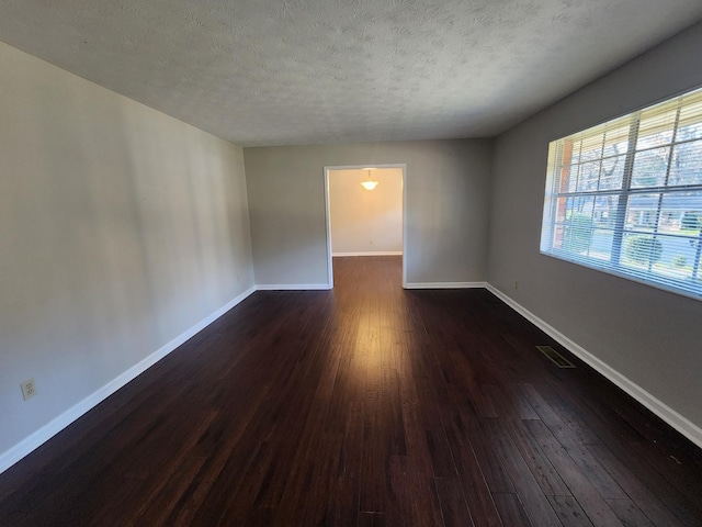 empty room with dark wood-type flooring, visible vents, a textured ceiling, and baseboards