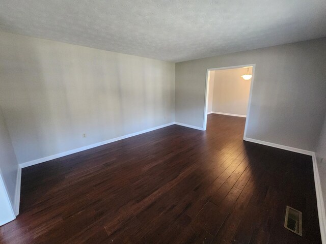 empty room with visible vents, dark wood finished floors, a textured ceiling, and baseboards