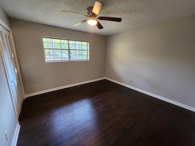 spare room featuring a textured ceiling, dark wood-type flooring, a ceiling fan, visible vents, and baseboards