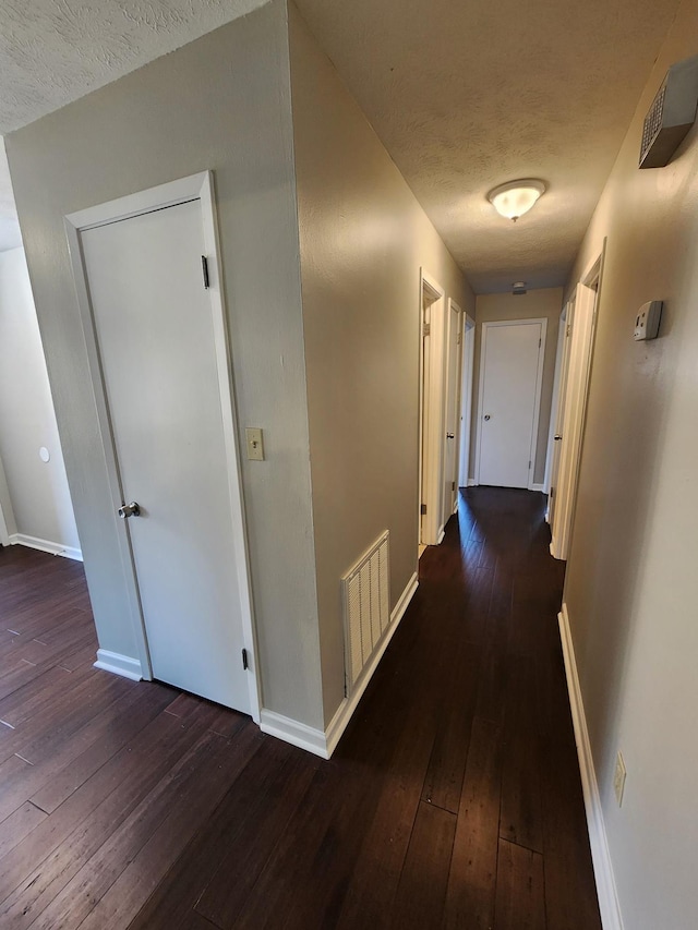 hall with wood-type flooring, visible vents, a textured ceiling, and baseboards