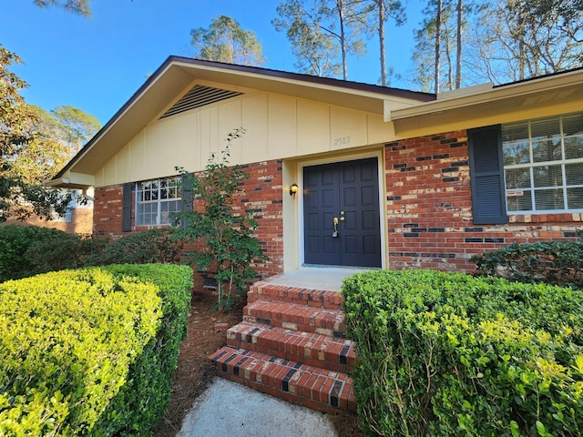 doorway to property featuring board and batten siding and brick siding