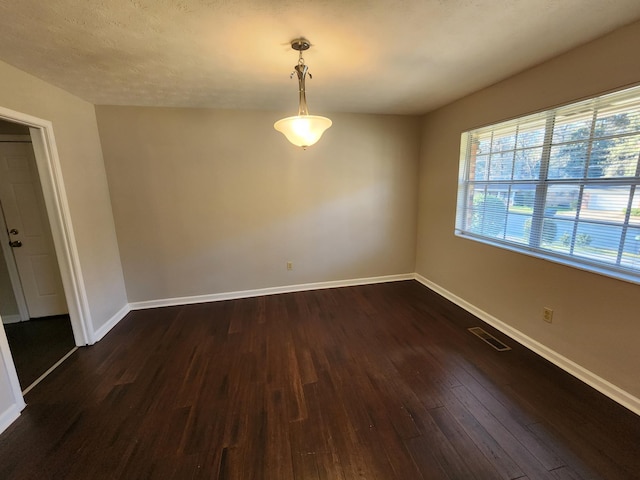 empty room with dark wood-style flooring, visible vents, a textured ceiling, and baseboards