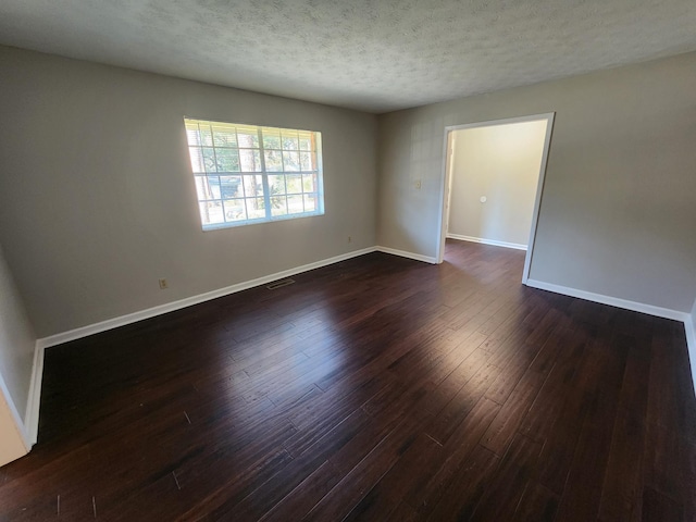 spare room with baseboards, a textured ceiling, visible vents, and dark wood-type flooring