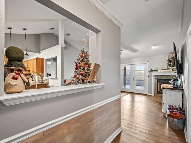 kitchen with vaulted ceiling, decorative light fixtures, ornamental molding, light hardwood / wood-style floors, and french doors