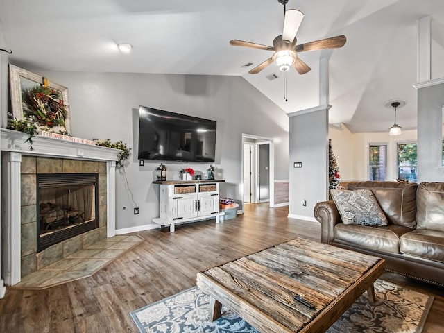 living room with vaulted ceiling, ceiling fan, a tiled fireplace, and hardwood / wood-style floors