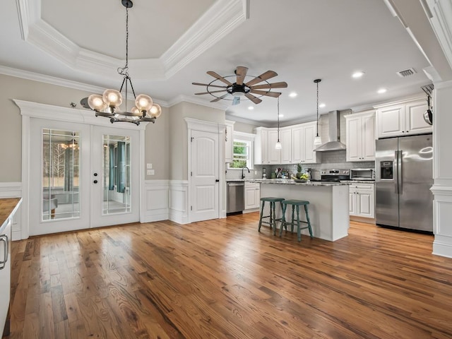 kitchen with pendant lighting, appliances with stainless steel finishes, a breakfast bar area, and wall chimney range hood