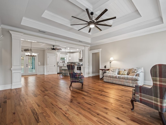 living room featuring a tray ceiling, ceiling fan with notable chandelier, and decorative columns