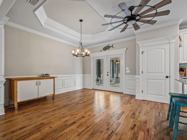 interior space with crown molding, a tray ceiling, ceiling fan with notable chandelier, and light wood-type flooring