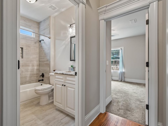 full bathroom with tiled shower / bath, vanity, toilet, and plenty of natural light