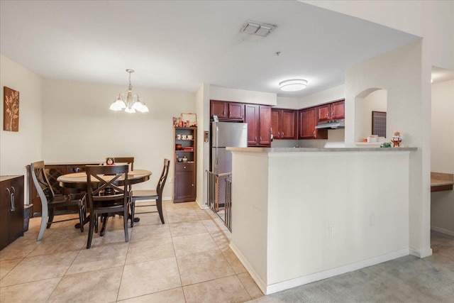 kitchen with under cabinet range hood, light countertops, visible vents, pendant lighting, and reddish brown cabinets