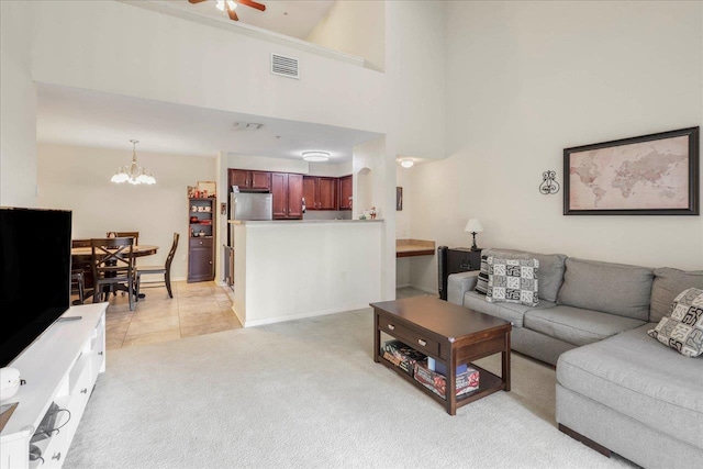 living room with visible vents, light carpet, baseboards, a towering ceiling, and ceiling fan with notable chandelier