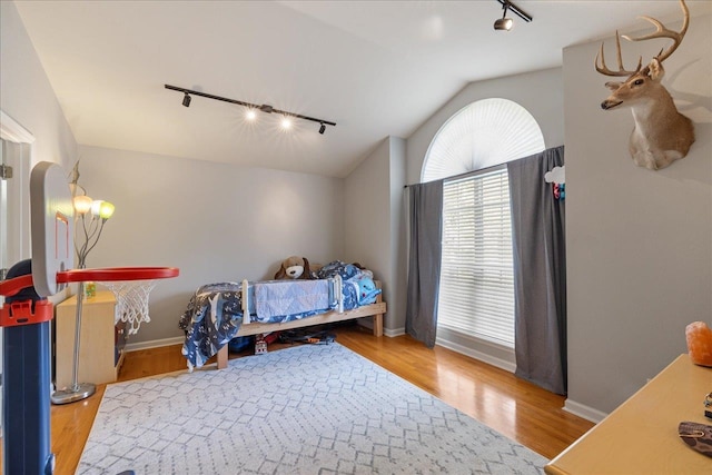 bedroom with hardwood / wood-style floors, rail lighting, and lofted ceiling