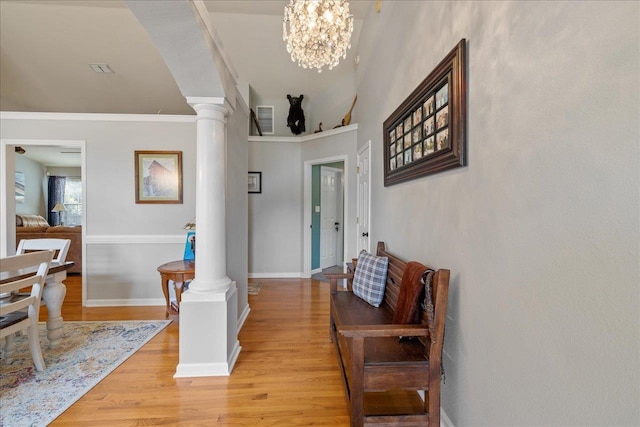 foyer entrance featuring decorative columns, crown molding, a chandelier, and light wood-type flooring