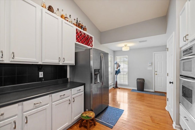 kitchen with backsplash, white cabinetry, light hardwood / wood-style flooring, and appliances with stainless steel finishes