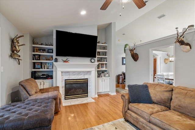 living room featuring ceiling fan, light wood-type flooring, lofted ceiling, and a tiled fireplace