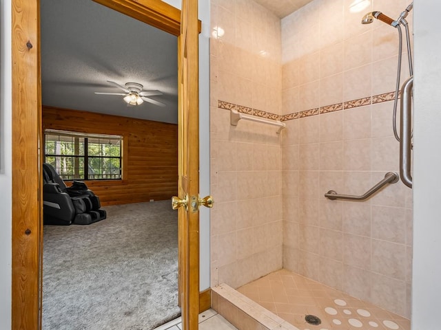 bathroom featuring ceiling fan, wooden walls, a textured ceiling, and a tile shower