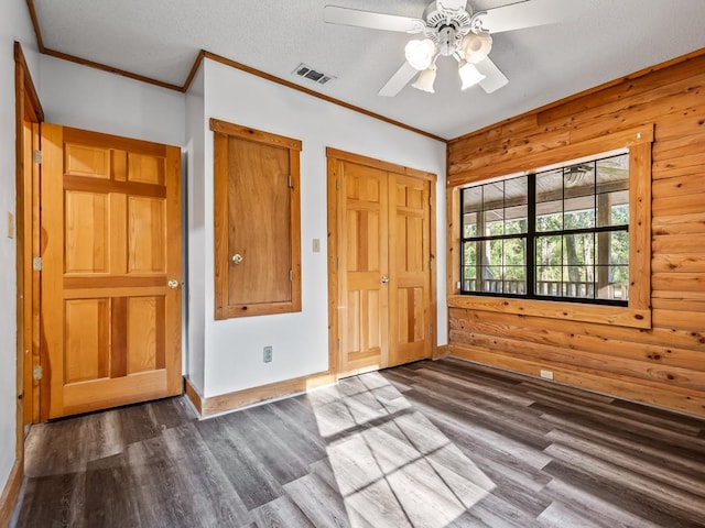 unfurnished bedroom with wood walls, ornamental molding, ceiling fan, a closet, and dark hardwood / wood-style flooring